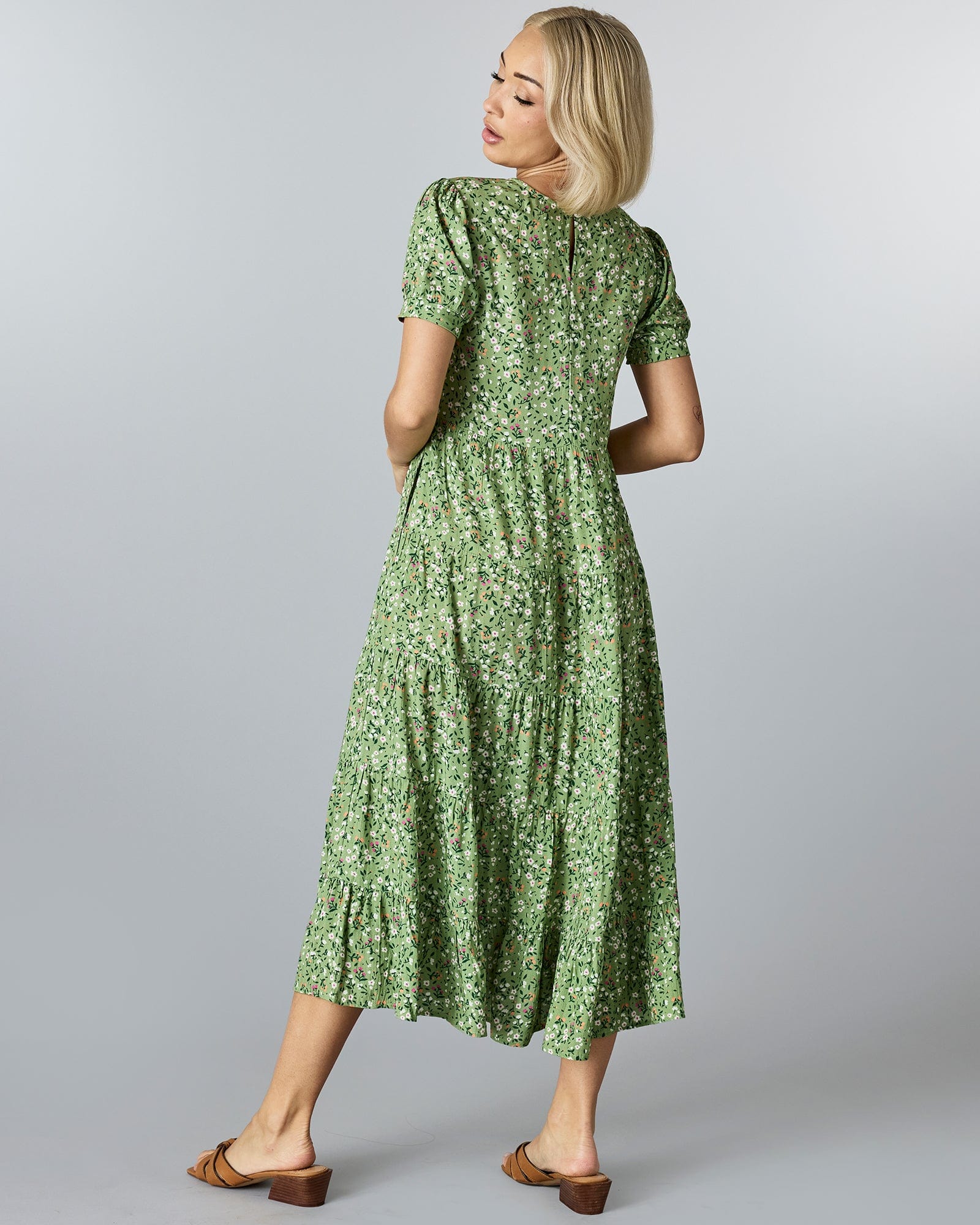 Woman in a green floral dress that has short sleeves and tiers down the skirt.