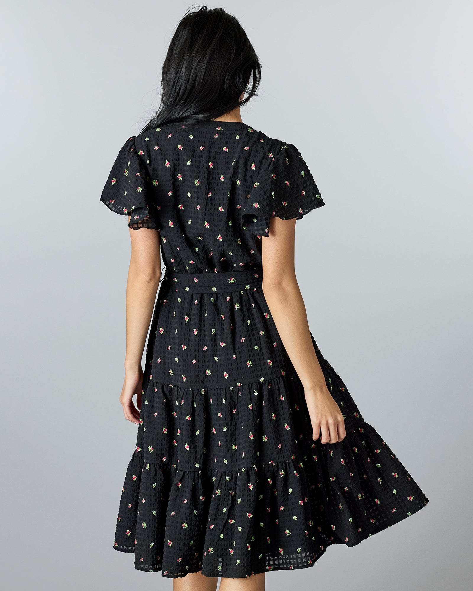 Woman in a black, floral print midi-length dress with a v-neck and short sleeves.