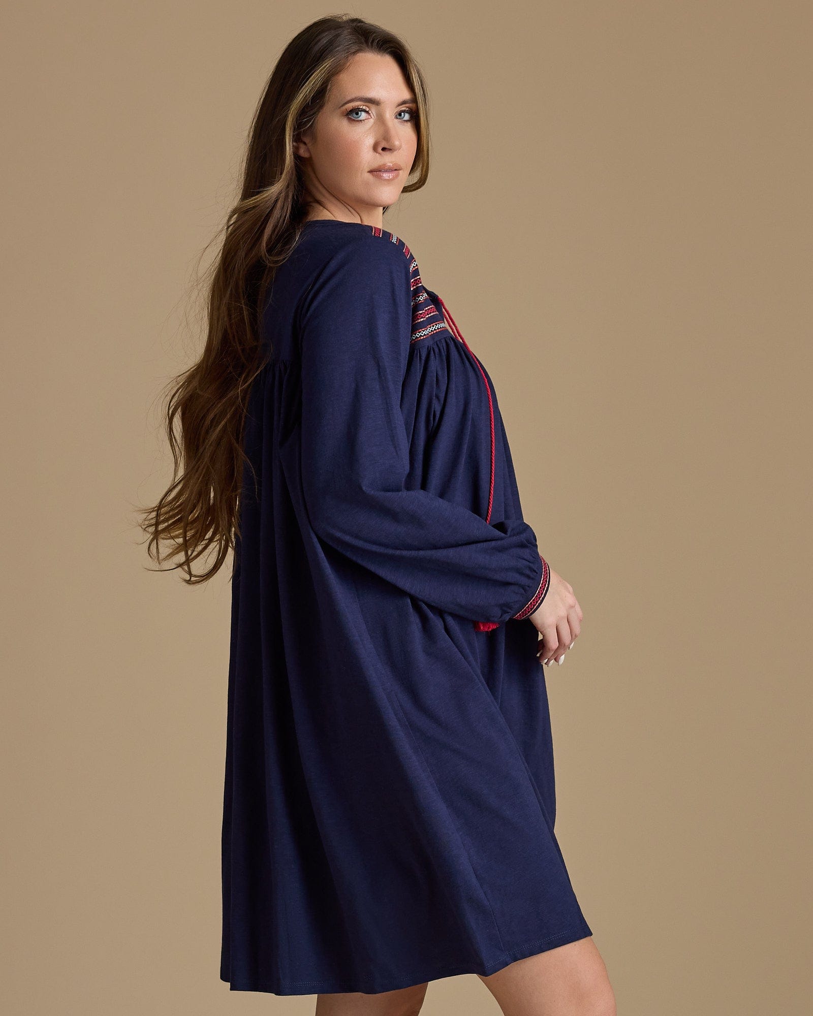 Woman in a long sleeve, knee-length, navy dress with red tassels