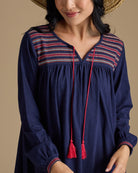 Woman in a long sleeve, knee-length, navy dress with red tassels