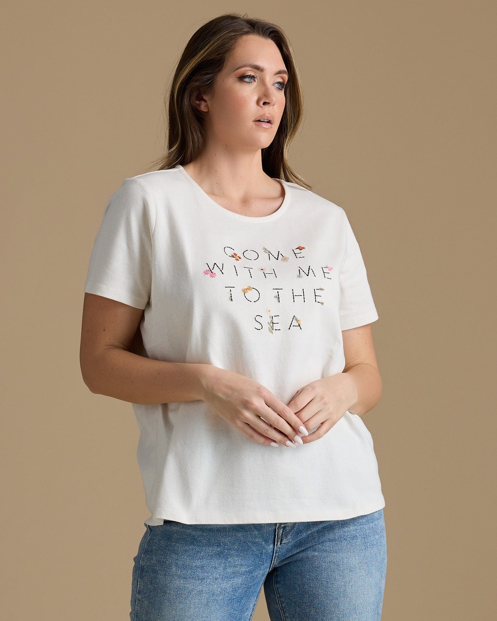 Woman in a white graphic tee that says "ccome with me to the sea"