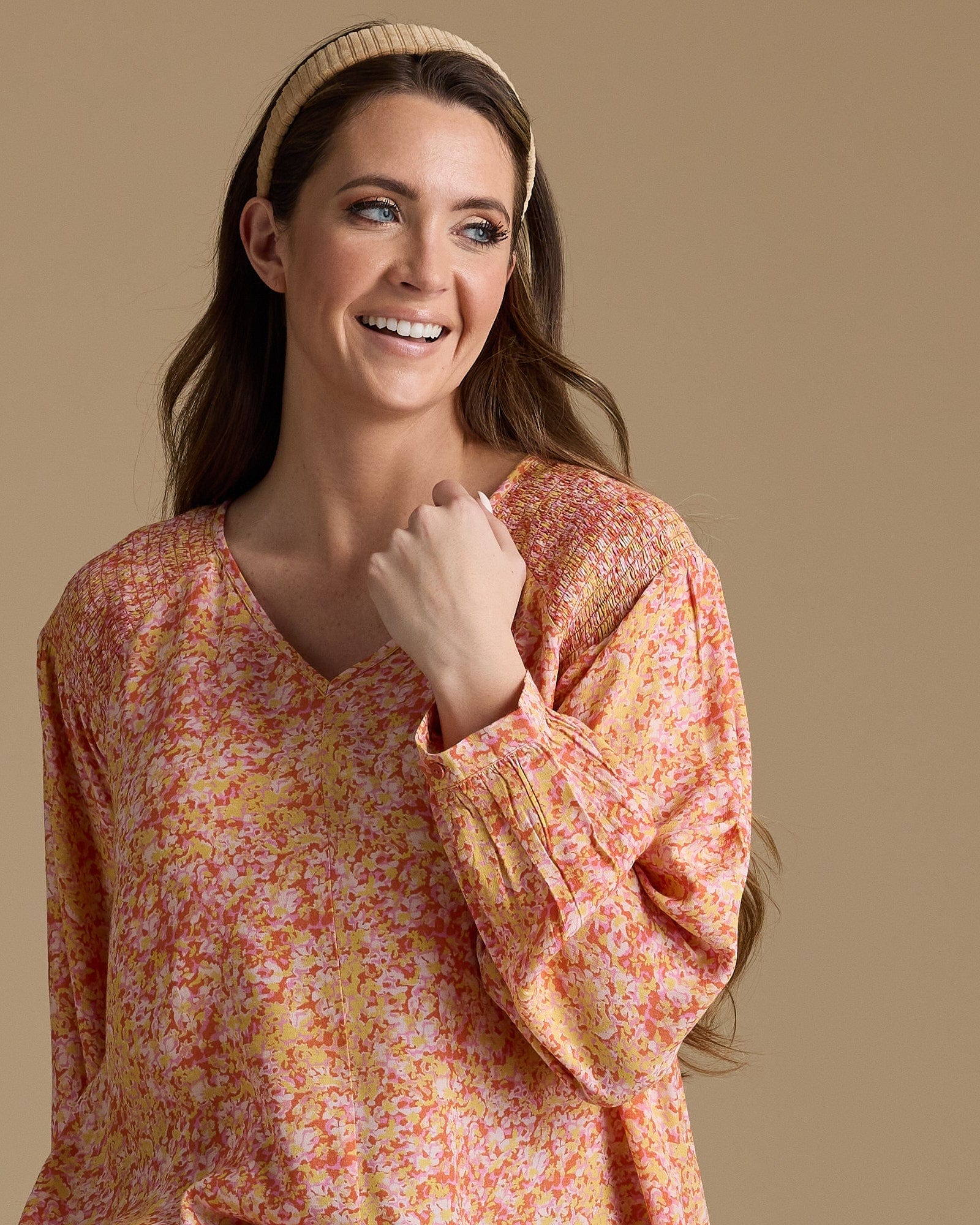 Woman in an orange, yellow and pink blouse with long sleeves