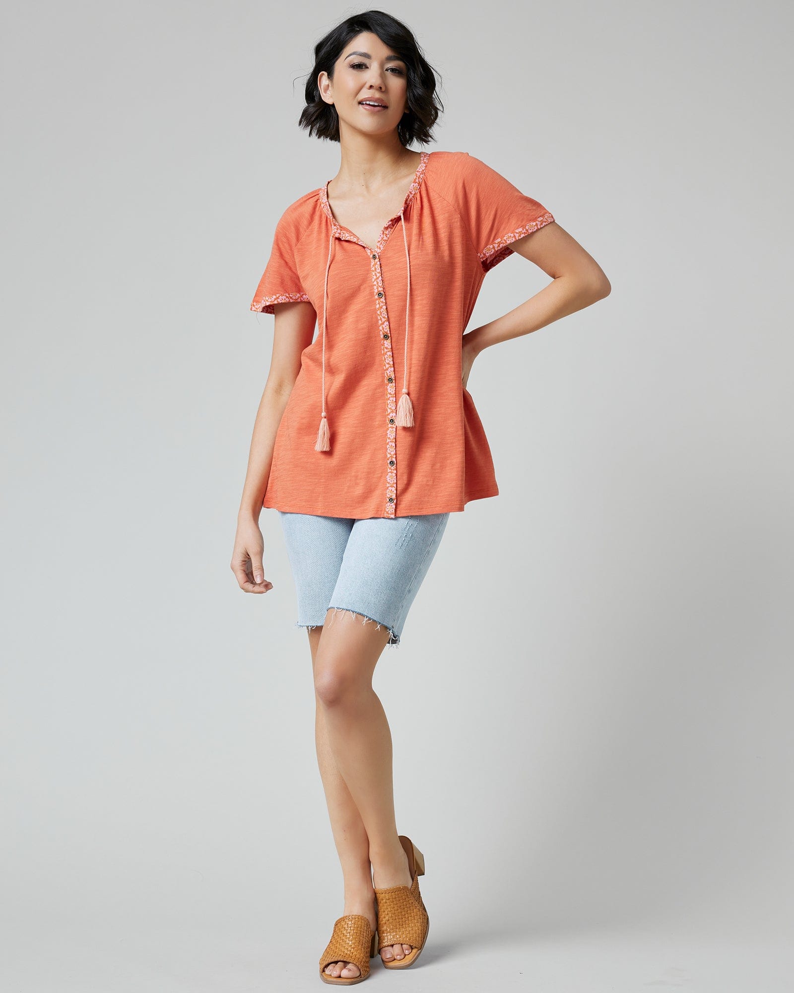 Woman in an orange top with short sleeves and buttons down the front