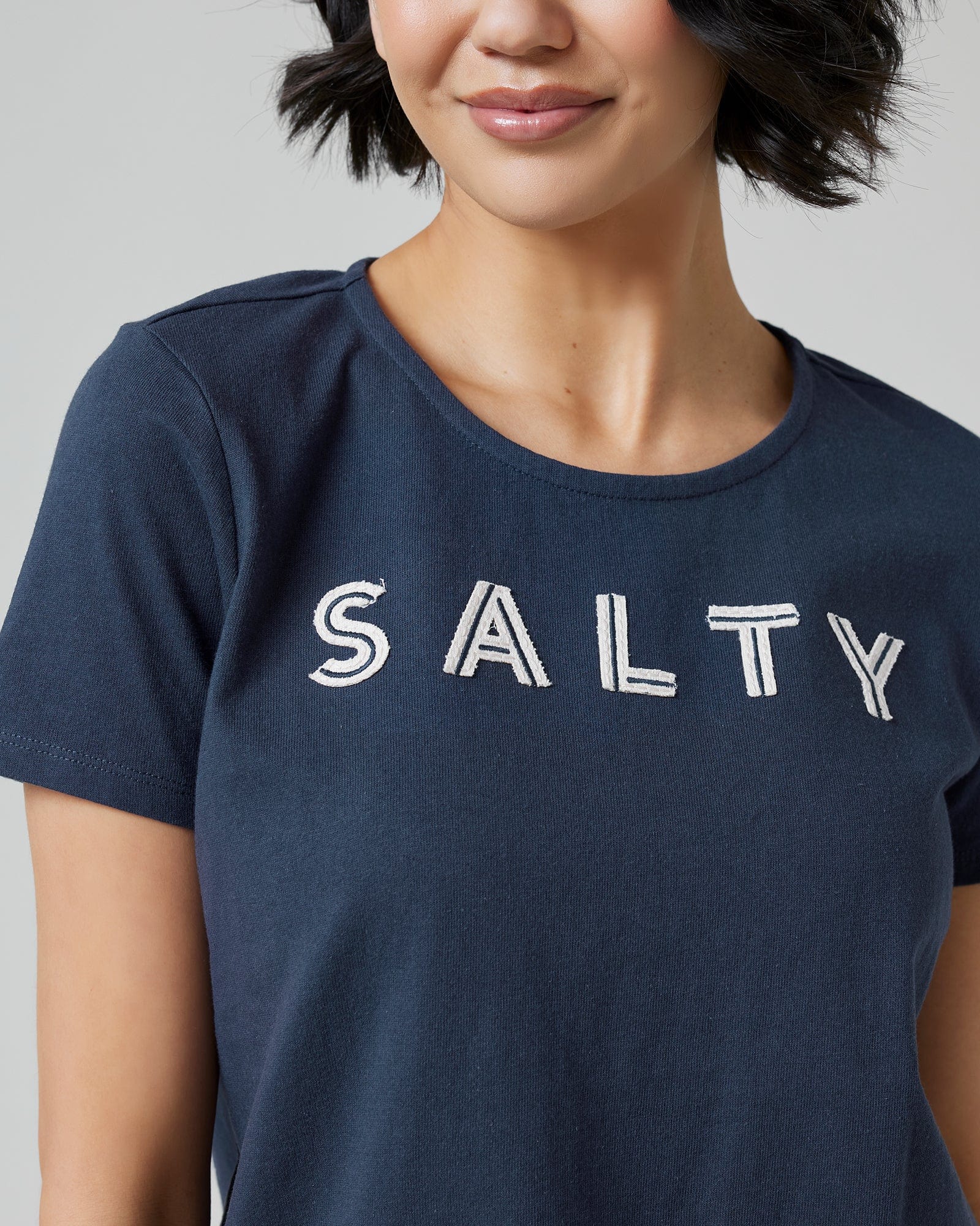 Woman in a navy graphic t-shirt with "SALTY" across the front