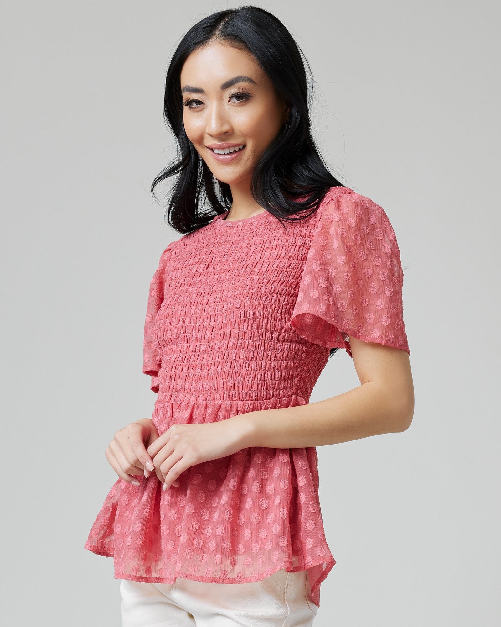 Woman in a pink peplum blouse with short sleeves, smocking and polka dots